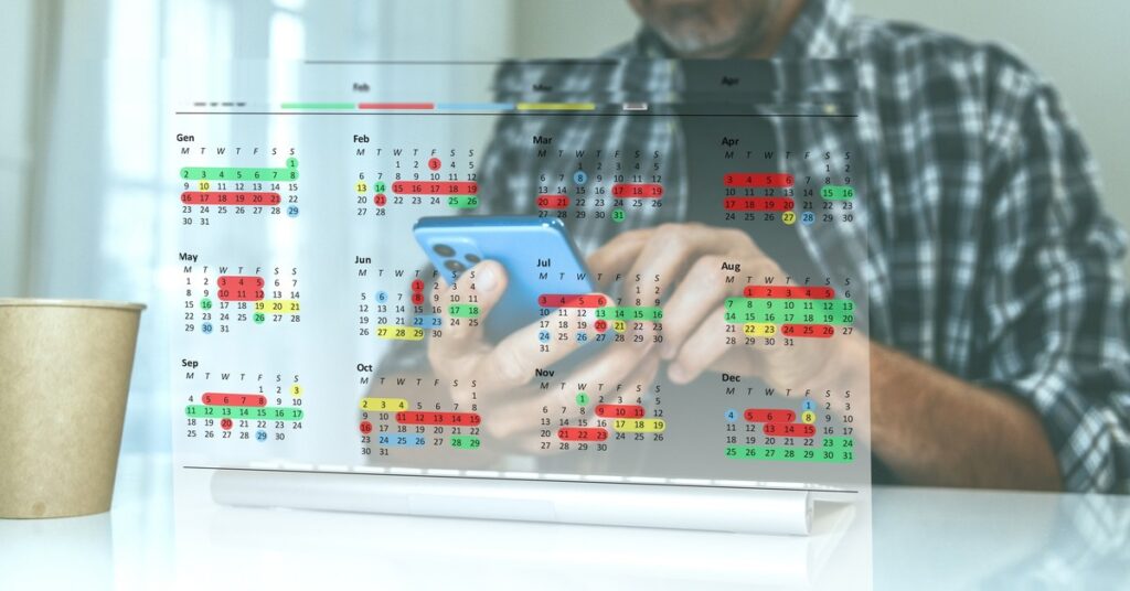 Color-coded annual calendar with person checking phone for schedule and travel planning